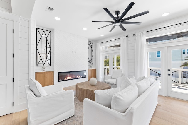 living room with ceiling fan, french doors, light hardwood / wood-style flooring, and a large fireplace