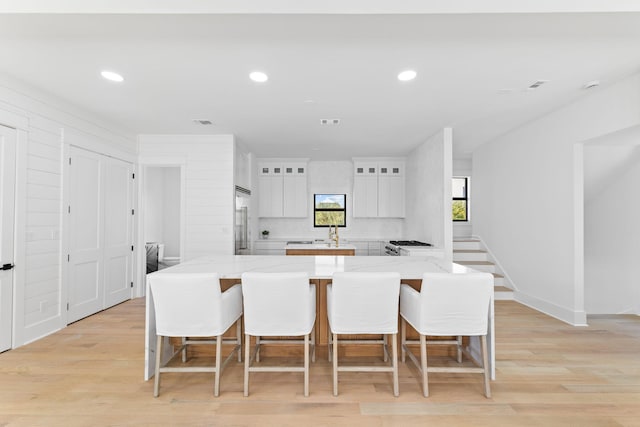 kitchen with built in refrigerator, light stone counters, light wood-type flooring, and white cabinetry