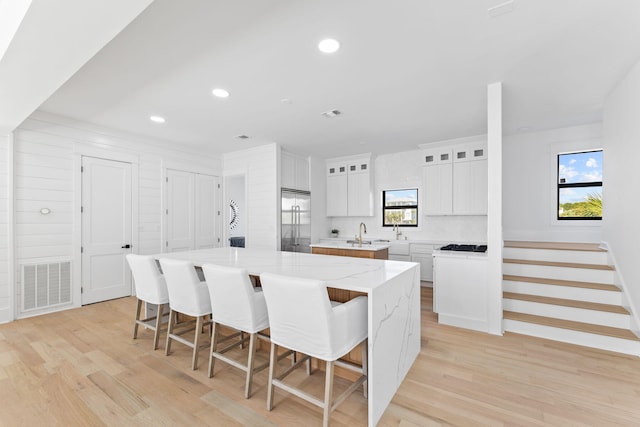 kitchen with white cabinetry, stainless steel built in refrigerator, a kitchen island, light hardwood / wood-style floors, and light stone countertops