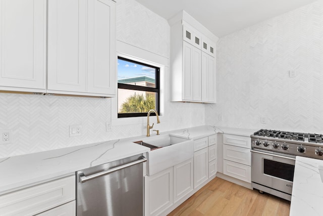 kitchen with appliances with stainless steel finishes, sink, light hardwood / wood-style floors, light stone countertops, and white cabinetry