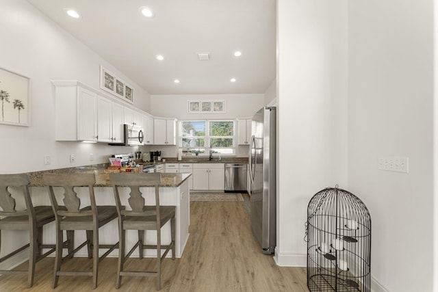 kitchen featuring kitchen peninsula, appliances with stainless steel finishes, a kitchen breakfast bar, dark stone countertops, and white cabinetry