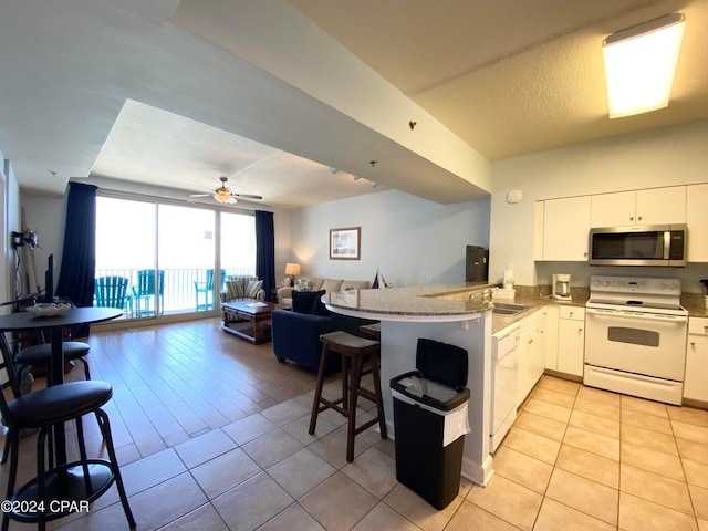 kitchen with a kitchen bar, white appliances, kitchen peninsula, and white cabinetry