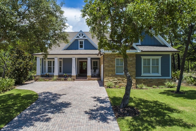 view of front of property with stone siding, a front lawn, a porch, and decorative driveway