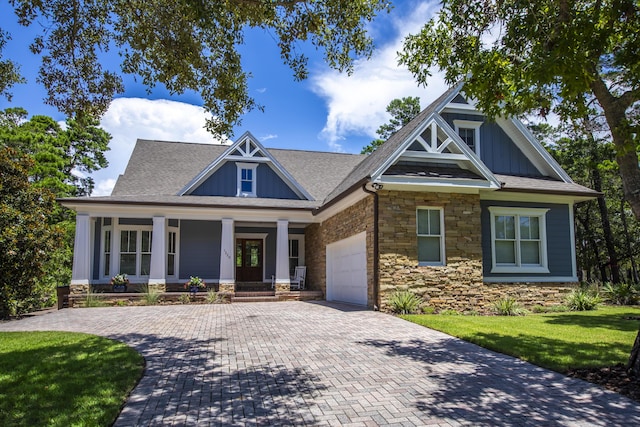 craftsman inspired home featuring decorative driveway, a porch, board and batten siding, a front yard, and a garage