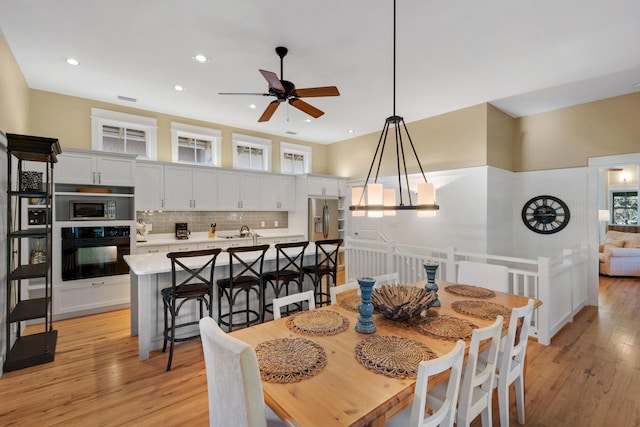 dining space featuring ceiling fan with notable chandelier, light wood-type flooring, and sink