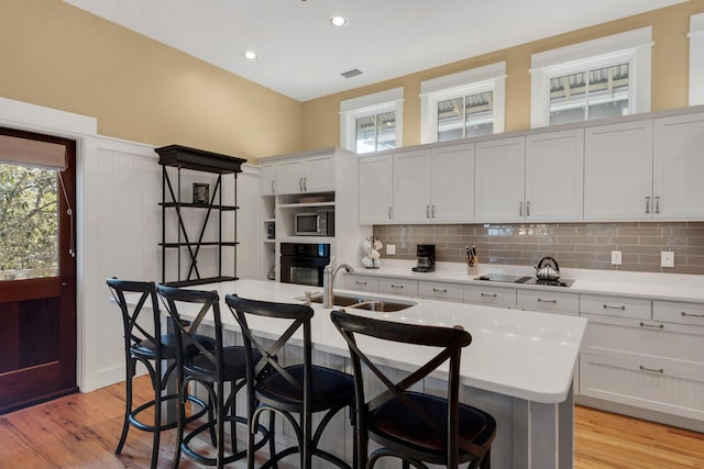 kitchen featuring sink, white cabinets, tasteful backsplash, black appliances, and a kitchen island with sink