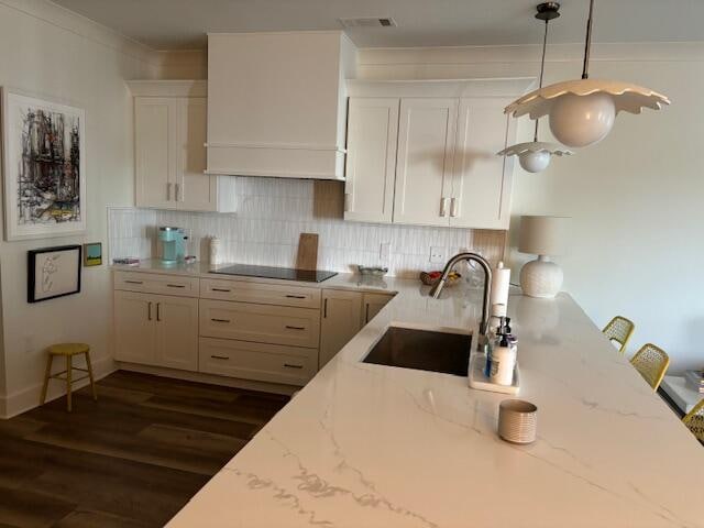 kitchen featuring tasteful backsplash, light stone countertops, sink, black electric stovetop, and decorative light fixtures