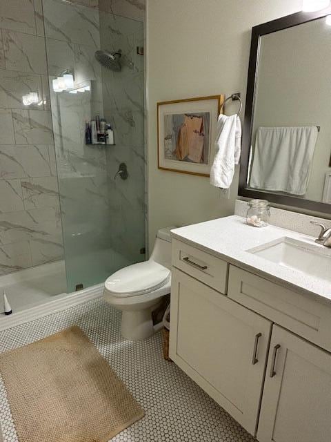 bathroom featuring a shower with shower door, vanity, tile patterned floors, and toilet