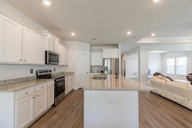 kitchen featuring white cabinetry, appliances with stainless steel finishes, a kitchen island with sink, and light stone counters