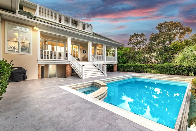 pool at dusk featuring an in ground hot tub and a patio