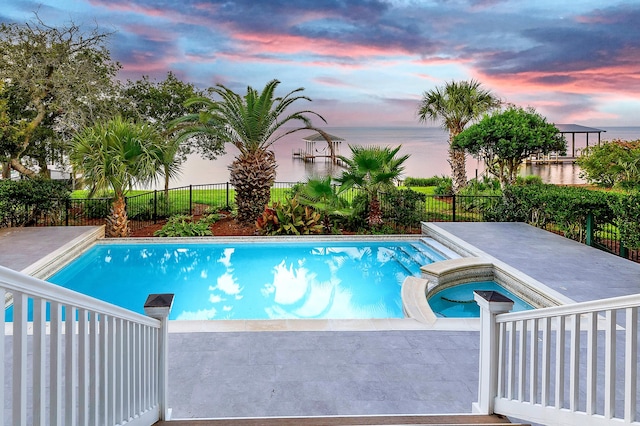 pool at dusk with an in ground hot tub and a water view