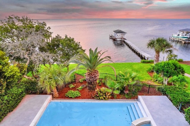 pool at dusk featuring a water view, a yard, and a boat dock