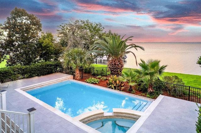 pool at dusk with an in ground hot tub and a water view