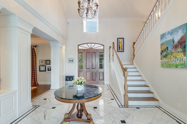 entrance foyer featuring an inviting chandelier, a towering ceiling, ornamental molding, and decorative columns