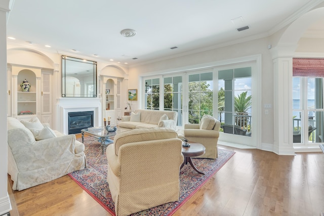 living room featuring ornate columns, ornamental molding, hardwood / wood-style floors, and built in features