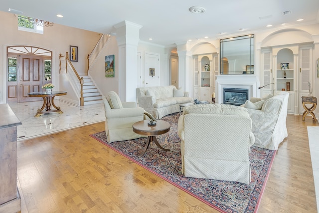 living room featuring decorative columns, crown molding, built in features, and light hardwood / wood-style flooring