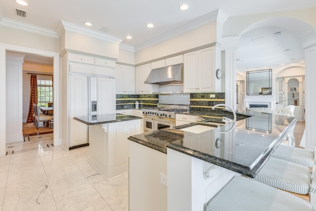 kitchen featuring high end appliances, a kitchen breakfast bar, dark stone counters, and a kitchen island