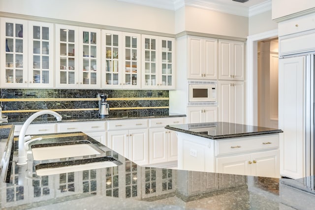 kitchen with ornamental molding, dark stone counters, built in appliances, and white cabinets