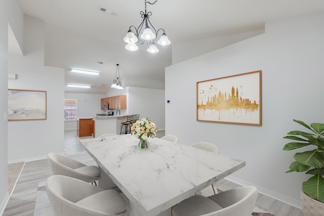 dining space with a notable chandelier, light wood-type flooring, and vaulted ceiling