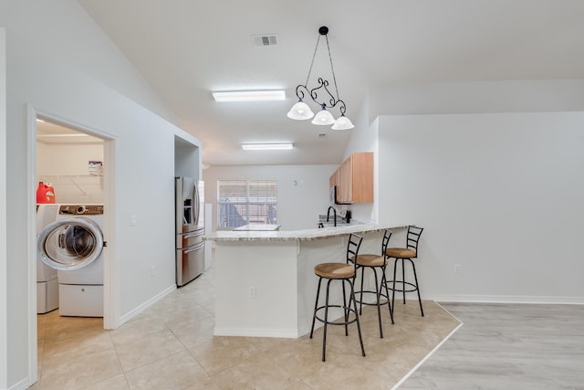 kitchen with kitchen peninsula, washer / clothes dryer, stainless steel fridge, a breakfast bar area, and pendant lighting