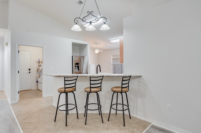 kitchen featuring a breakfast bar area, pendant lighting, washing machine and clothes dryer, and stainless steel refrigerator with ice dispenser