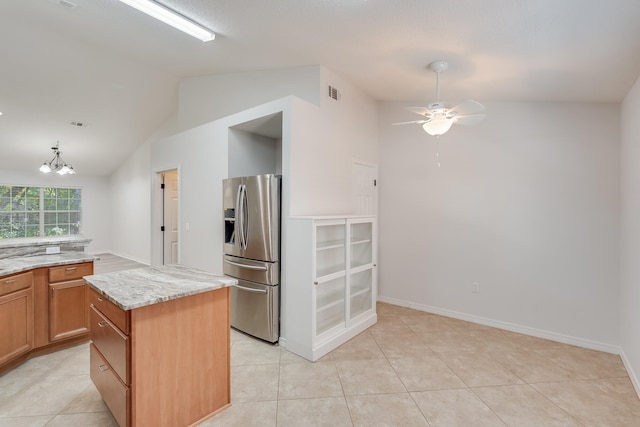 kitchen featuring lofted ceiling, stainless steel fridge, light stone countertops, ceiling fan with notable chandelier, and a center island