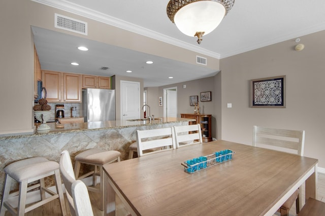 dining room featuring sink, light wood-type flooring, and ornamental molding