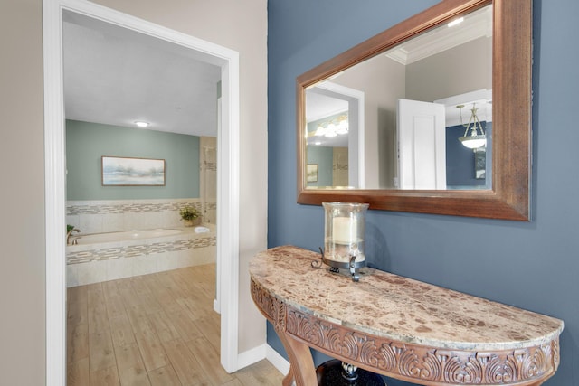 bathroom with crown molding, hardwood / wood-style floors, and a relaxing tiled tub