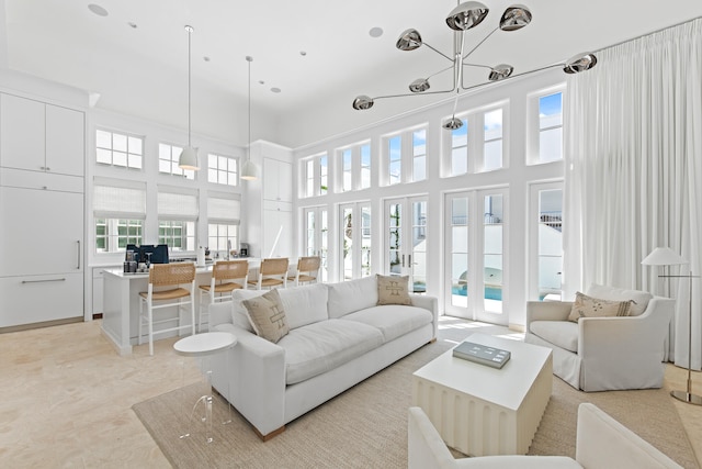 living room with plenty of natural light, an inviting chandelier, a towering ceiling, and french doors