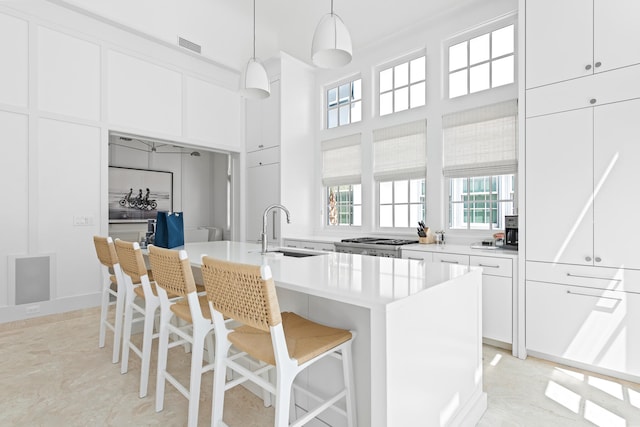 kitchen featuring a kitchen island with sink, white cabinets, decorative light fixtures, sink, and light tile patterned flooring