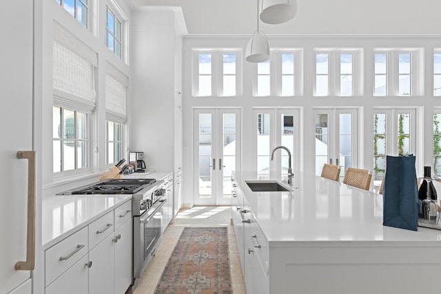 kitchen featuring high end stainless steel range, white cabinetry, a healthy amount of sunlight, and an island with sink