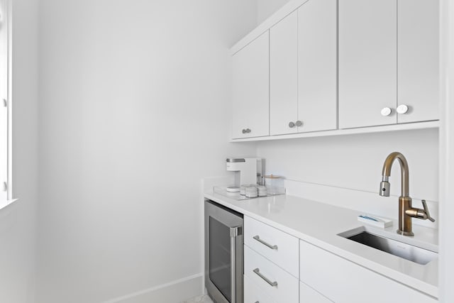 kitchen with beverage cooler, white cabinetry, and sink