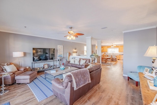 living area featuring visible vents, light wood-style floors, crown molding, baseboards, and ceiling fan