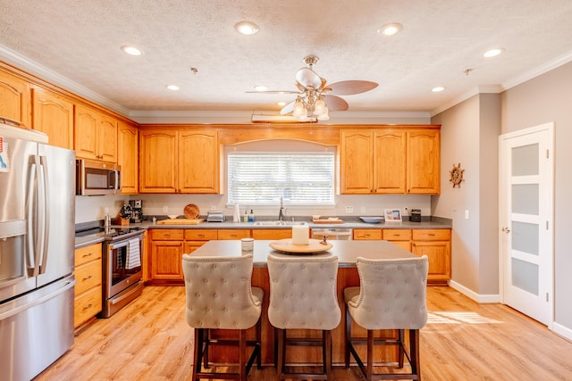 kitchen featuring a sink, a kitchen island, light wood-style floors, appliances with stainless steel finishes, and a breakfast bar area