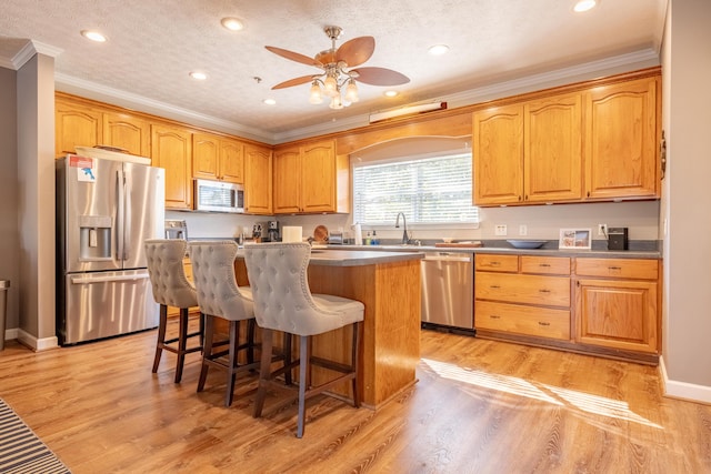 kitchen with a center island, crown molding, light wood-style flooring, a kitchen breakfast bar, and stainless steel appliances