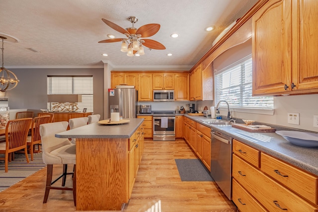 kitchen with a center island, crown molding, appliances with stainless steel finishes, a kitchen breakfast bar, and a sink