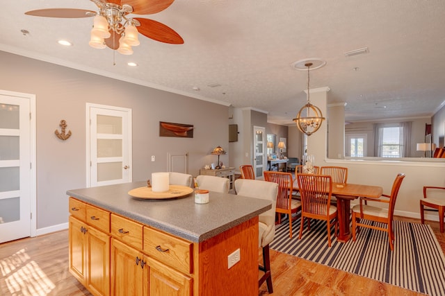 kitchen with crown molding, dark countertops, light wood-type flooring, and a center island