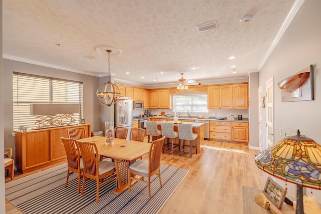 dining space featuring baseboards, visible vents, a textured ceiling, crown molding, and light wood-type flooring