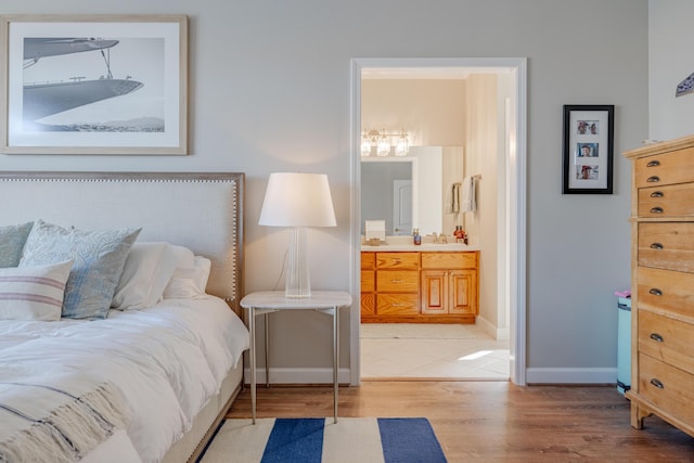 bedroom featuring a sink, baseboards, light wood-style flooring, and ensuite bathroom