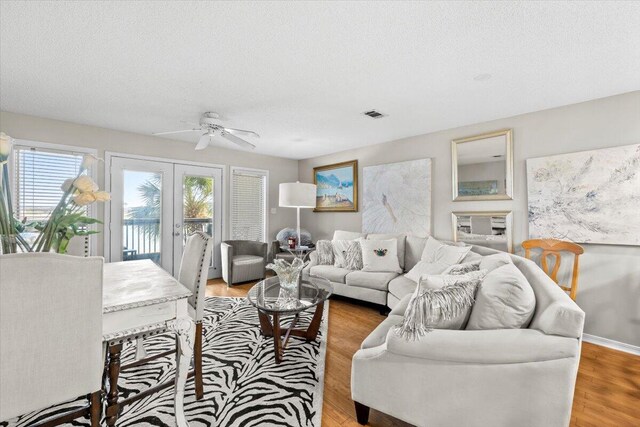 living area with a textured ceiling, french doors, light wood finished floors, and visible vents