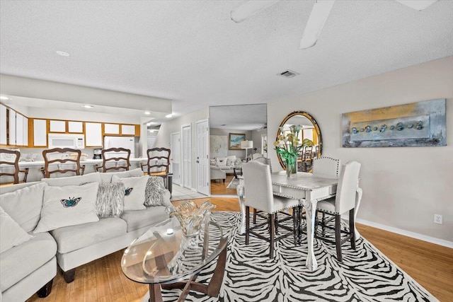 living area featuring light wood-type flooring, visible vents, a textured ceiling, and baseboards