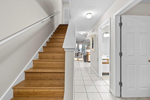 stairs with tile patterned flooring, baseboards, and a textured ceiling