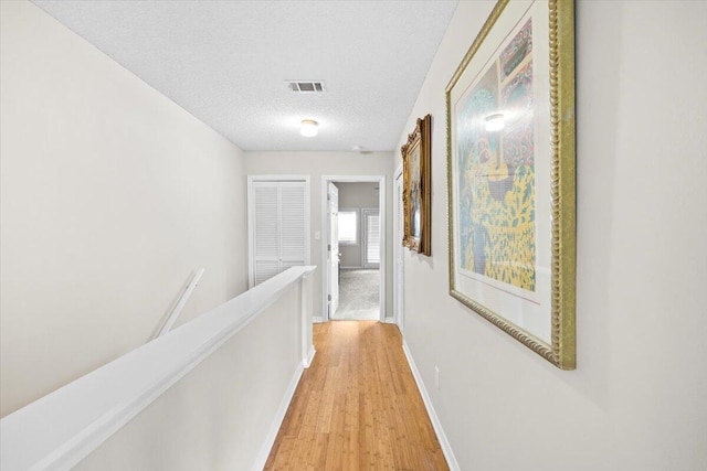 hallway with baseboards, visible vents, a textured ceiling, an upstairs landing, and light wood-style floors