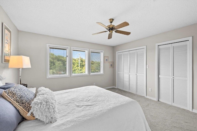 bedroom with baseboards, a ceiling fan, carpet, a textured ceiling, and two closets