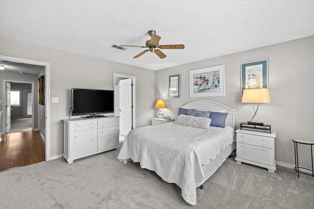 bedroom featuring baseboards, visible vents, light carpet, and a textured ceiling