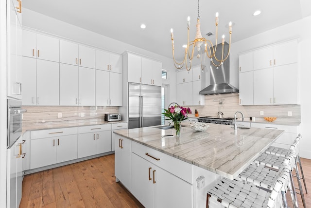 kitchen with light hardwood / wood-style floors, a center island with sink, appliances with stainless steel finishes, a kitchen breakfast bar, and white cabinets