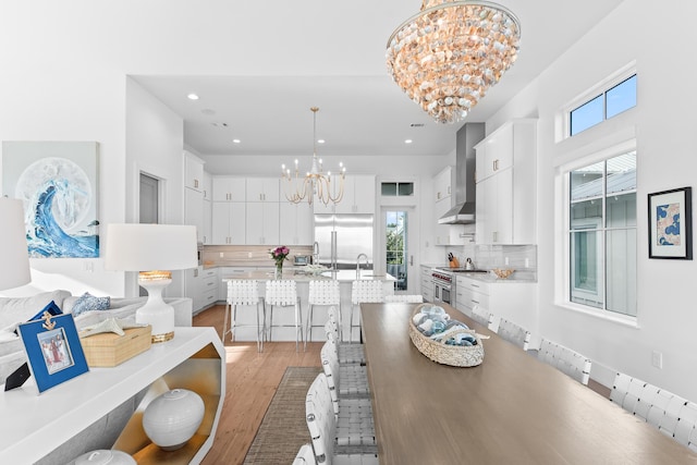 kitchen featuring white cabinets, wall chimney exhaust hood, high end appliances, hanging light fixtures, and a chandelier