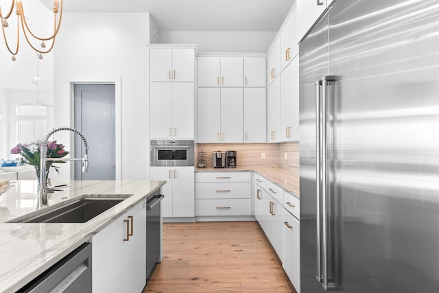 kitchen featuring white cabinetry, appliances with stainless steel finishes, backsplash, decorative light fixtures, and sink