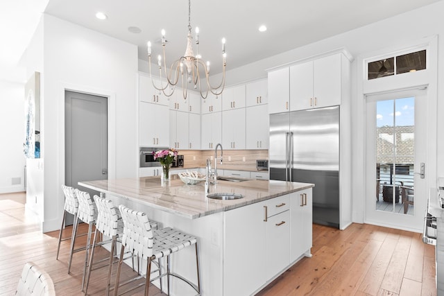 kitchen with stainless steel appliances, white cabinets, hanging light fixtures, and an island with sink