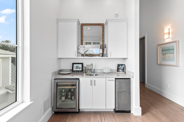 bar with wine cooler, sink, light wood-type flooring, white cabinets, and stainless steel fridge